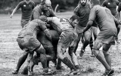 grayscale photography of group of people playing rugby on muddy field